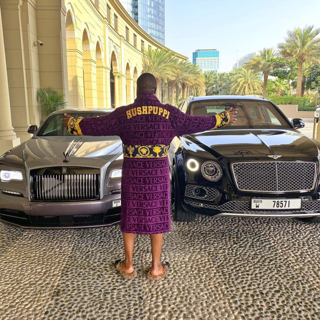 Image taken from "Hushpuppi" (cybercriminal caught conducting social engineering scams) posing in front of luxury cars with a custom designer robe.