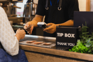 Person handing cashier their credit card to purchase something from a coffee shop. The cashier is using a card reader.